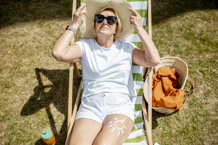 Beautiful senior woman in white clothes lying on the sunbed, relaxing in the park. Concept of rest...
