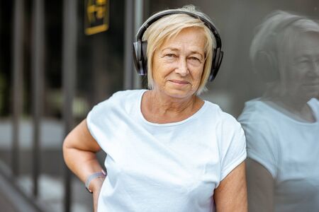Portrait of an active senior woman in sports clothes standing with headphones outdoors. Concept of a healthy lifestyle on retirementの写真素材
