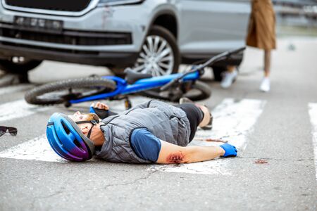 Road accident with injured cyclist lying on the pedestrian crossing near the broken bicycle and worried woman driver and car on the backgroundの写真素材