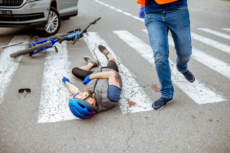 Road accident with injured cyclist lying on the pedestrian crossing near the broken bicycle and car driver running on the backgroundの写真素材