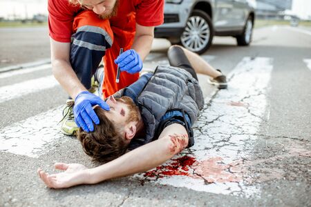 Medic checking unconscious person with flashlight, applying first aid to the bleeding person on the road after the accident on the pedestrian crossingの写真素材