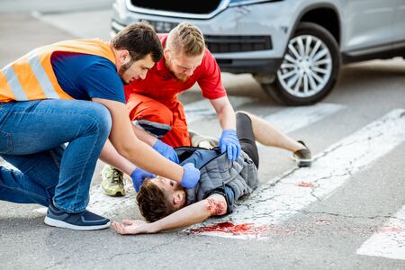 Medic with car driver applying first aid to the injured man lying on the pedestrian crossing after the road accidentの写真素材