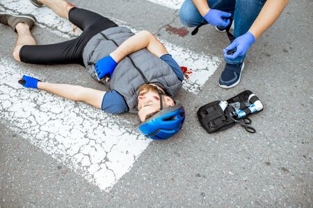 Road accident with injured cyclist on the pedestrian crossing with passerby pedestrian providing first aidの写真素材