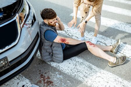 Woman driver with injured man talking phone, while suffering near the broken car on the pedestrian crossing after the accidentの写真素材