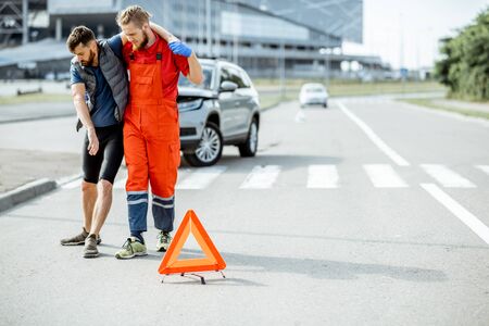 Medic in uniform helping injured man to walk, applying first aid after the road accidentの写真素材