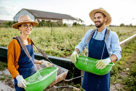 Portrait of a well-dressed farmers standing on the farmland with green buckets for feeding snails on a farm outdoors. Concept of agribusiness and farmingの写真素材