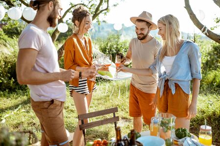 Young and cheerful friends having fun, drinking wine in the beautifully decorated backyard during a festive meeting or party on a sunny summer eveningの写真素材