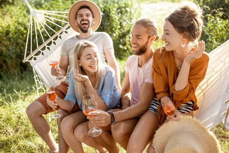 Portrait of a group of cheerful friends sitting together on the hammock, having fun outdoors during a summer daysの写真素材