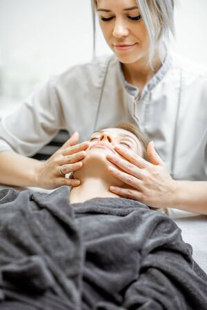 Cosmetologist making facial massage to a beautiful woman at the beauty salon. Concept of a lymph drainage therapyの写真素材