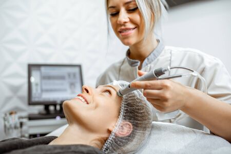 Cosmetologist making vacuum hydro peeling on the forehead region to a woman at the luxury beauty salon. Concept of a professional facial treatmentの写真素材