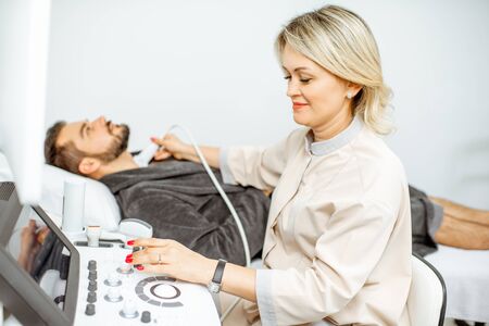 Female doctor performs ultrasound examination of a men's thyroid in the medical office. Concept of ultrasound diagnostics of male healthの写真素材