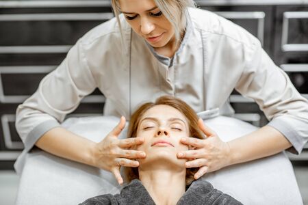 Cosmetologist making facial massage to a beautiful woman at the beauty salon. Concept of a lymph drainage therapyの写真素材