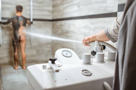 Man having high pressure shower after the mud wrapping procedure at the luxury SPA salon. Concept of hydrotherapy and Sharko showerの写真素材