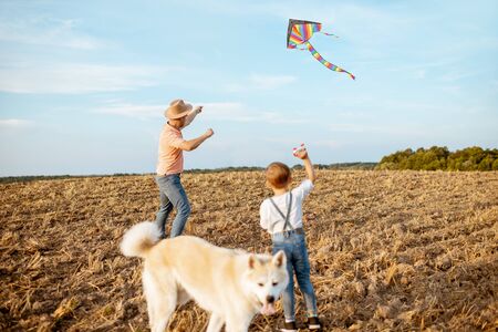 Father and son launching colorful air kite on the field, dog walking around. Concept of a happy family having fun during the summer activityの写真素材