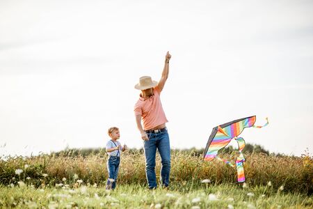 Father with son launching colorful air kite on the field during the sunset. Concept of a happy family having fun during the summer activityの写真素材