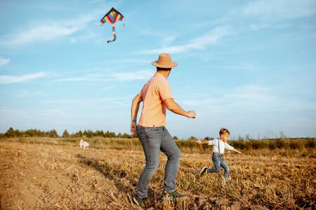 Father with son running while launching colorful air kite on the field. Concept of a happy family having fun during the summer activityの写真素材