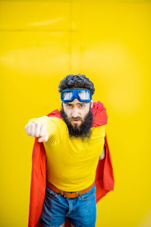 Portrait of a man like a superhero in colorful clothes and pilots glasses on the yellow backgroundの写真素材