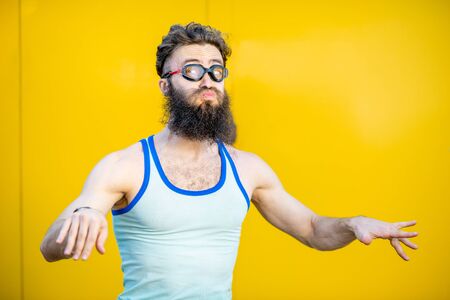 Portrait of a weird, old-fashioned swimmer dressed in 80s style with swimming glasses on the yellow backgroundの写真素材