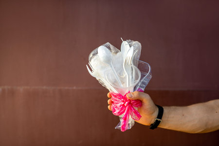 Man holding a bouquet made of plastic garbage on the dark red background. Concept of non-recyclable...