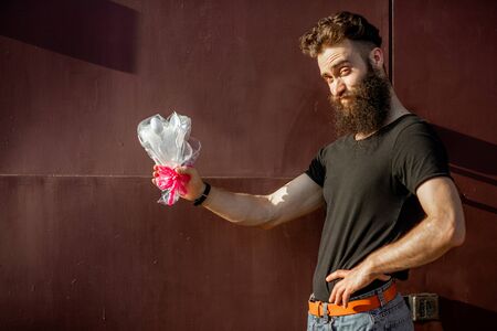 Man holding a bouquet made of plastic garbage on the dark red background. Concept of non-recyclable plastic pollutionの写真素材