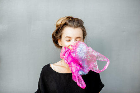 Portrait of a young woman suffocated of plastic bags on the grey background. Concept of...