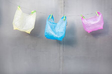 Three plastic bags hanging on the gray background. Concept of non-recyclable plastic pollutionの写真素材