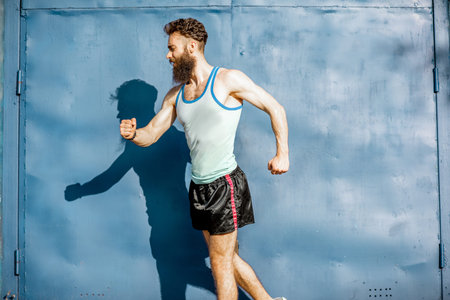 Funny portrait of an old-fashioned athlete dressed in 80s style posing on the blue wall background