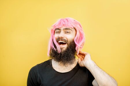 Funny portrait of a stylish playful man with beard and long color hair with expressive emotions on the yellow backgroundの写真素材