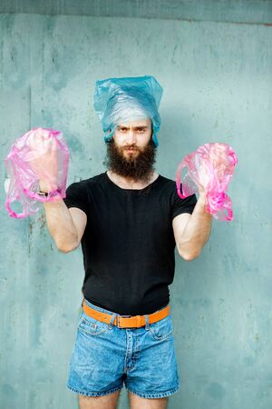 Portrait of confused man with plastic bags on hands and head standing on the green background. Concept of non-recyclable plastic pollutionの写真素材