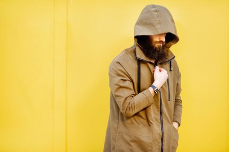 Portrait of a mysterious and weird man wearing hoodie coat on the yellow backgroundの写真素材