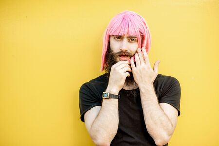 Funny portrait of a stylish playful man with beard and long color hair with expressive emotions on the yellow backgroundの写真素材
