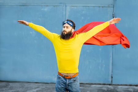 Portrait of a man like a superhero in colorful clothes and pilot's glasses on the blue backgroundの写真素材