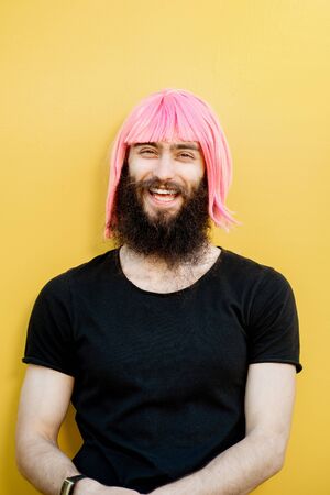 Funny portrait of a stylish playful man with beard and long color hair with expressive emotions on the yellow backgroundの写真素材