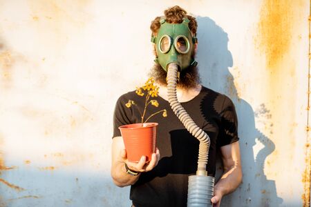 Portrait of a sad man with gas mask holding dried flowerpot on the grey rusty background. Concept of poor ecology, air pollution and radiation hazardsの写真素材