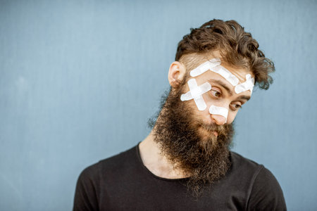 Close-up portrait of an injured man with medical patches on his face on the blue baackground