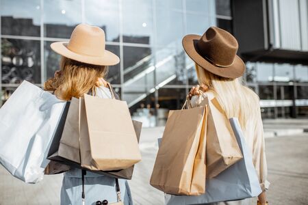 Two women wearing hats holding empty shopping bags with copy space, while standing back near the shopping mallの写真素材