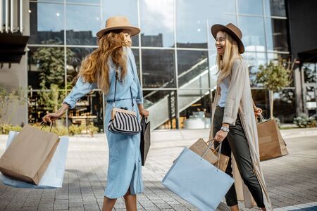 Portrait of two joyful and happy woman with shopping bags in front of the shopping mall, feeling excited with new purchasesの写真素材