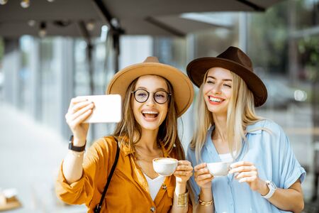 Two female best friends making selfie portrait while spending time together on the cafe terrace during a summer dayの写真素材