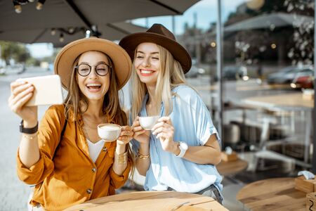 Two female best friends making selfie portrait while spending time together on the cafe terrace during a summer dayの写真素材