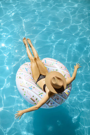 Woman in swimsuit and hat swimming with inflatable ring in the form of a donut in the water pool,...