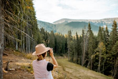 Young female traveler looking with binoculars while traveling in the mountains at the pine forestの写真素材