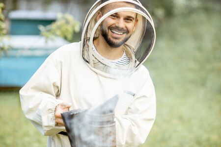 Portrait of a cheerful beekeeper in protective uniform with bee smoker on the apiaryの写真素材