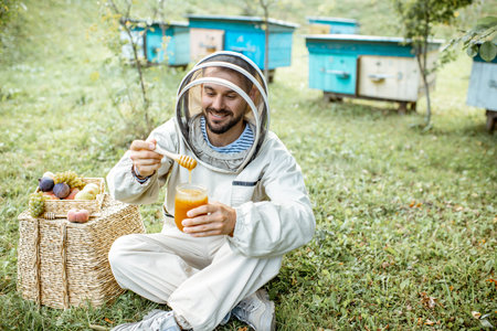 Portrait of a cheerful beekeeper in protective uniform with honey products and sweet fruits on the...
