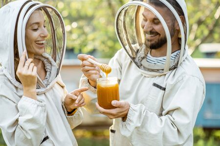 Beekepers in protective uniform with fresh honey in the jar, tasting product on the apiary outdoorsの写真素材