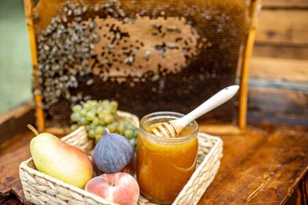 Composition of sweet fruits and jar with honey on the beehive with honeycomb on the backgroundの写真素材