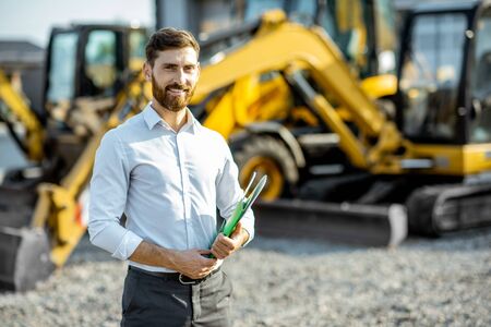 Portrait of a handsome sales consultant or manager standing on the open ground of the shop with heavy machinery for constructionの写真素材
