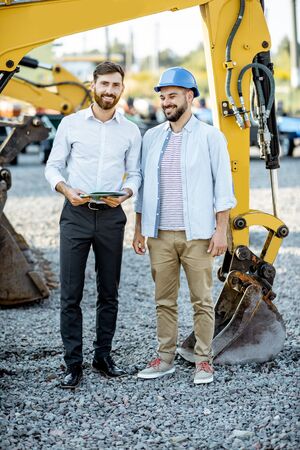 Builder choosing heavy machinery for construction, talking with a sales consultant on the open ground of a shop with special vehiclesの写真素材