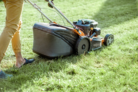 Gardener cutting grass with gasoline lawn mower on the backyard, close-up view