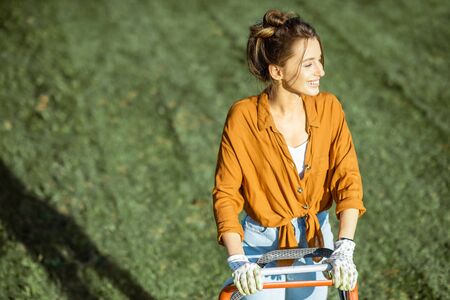 Portrait of a beautiful young woman cutting grass with gasoline lawn mower, gardening on the backyard in the countrysideの写真素材