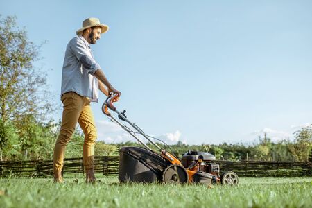 Handsome man dressed casually cutting grass with gasoline lawn mower enjoying gardening process on the backyardの素材 [FY310132232769]